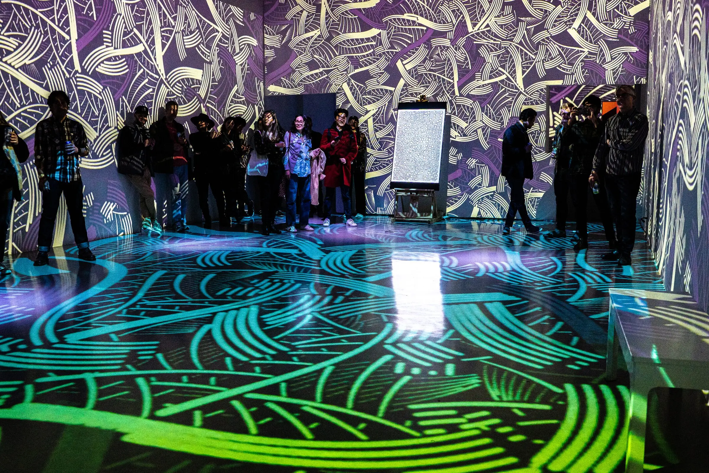 Le public dans une salle aux murs et au sol couverts de motifs projetés, pendant l'événement INTRICADA, Lume Studios, New York.
