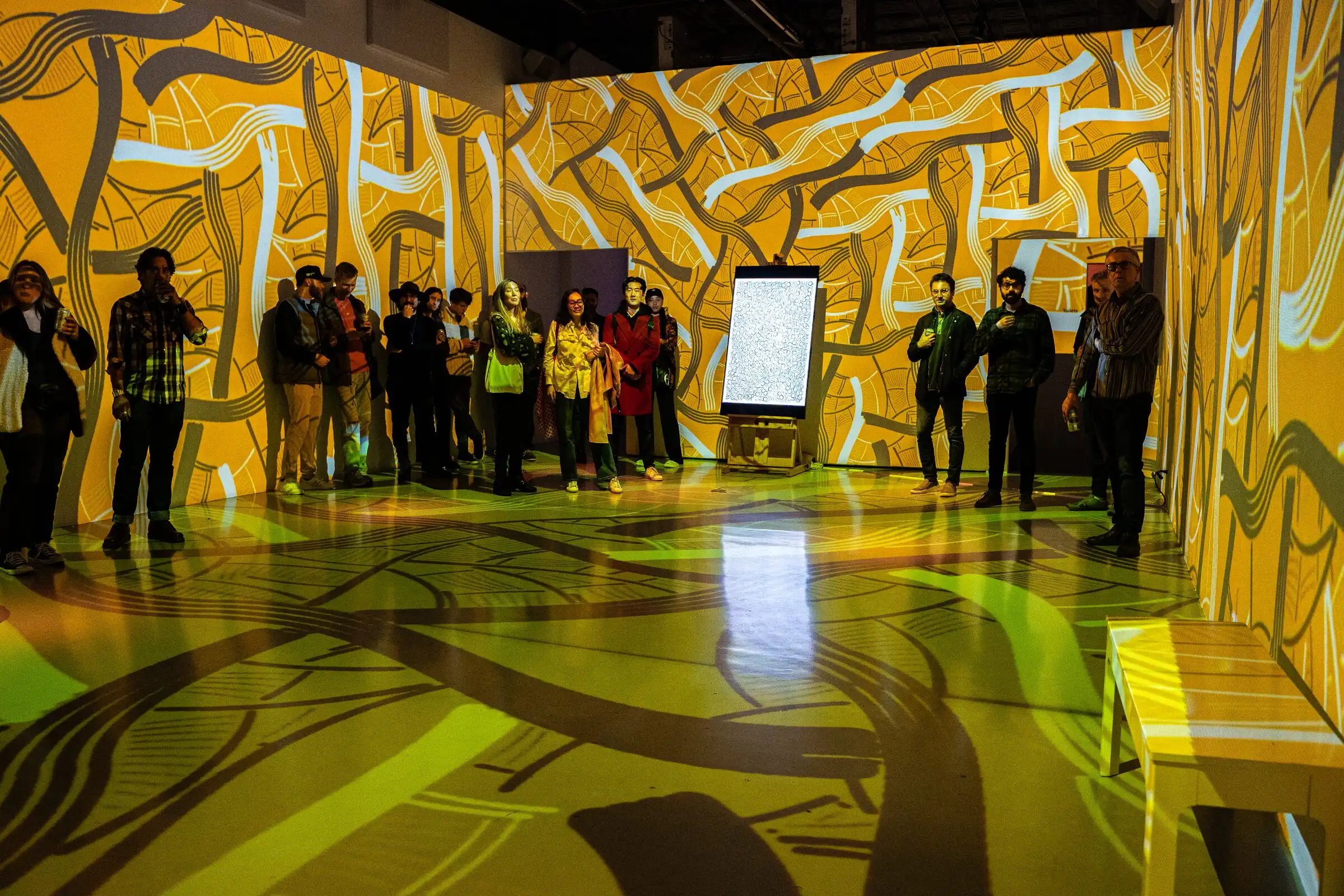 Visitors gathered around a room bathed in yellow projected patterns, Lume Studios, New York.