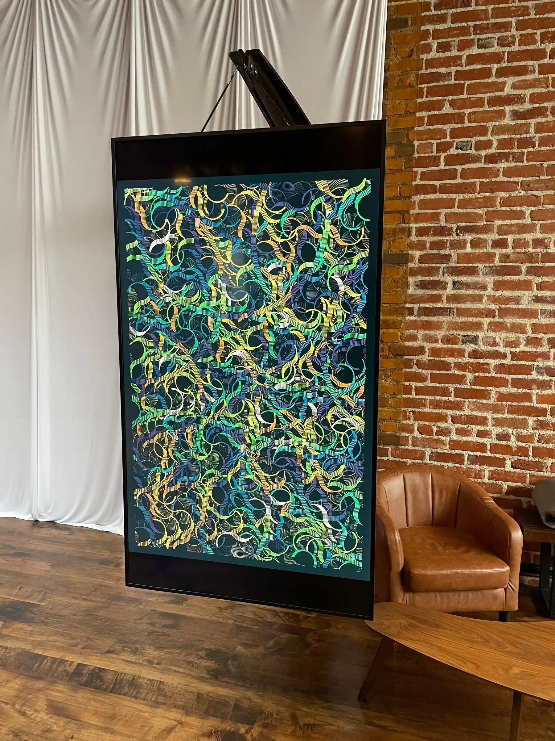 An INTRICADA screen hanging from a stand beside a brick wall, Bright Moments Los Angeles.