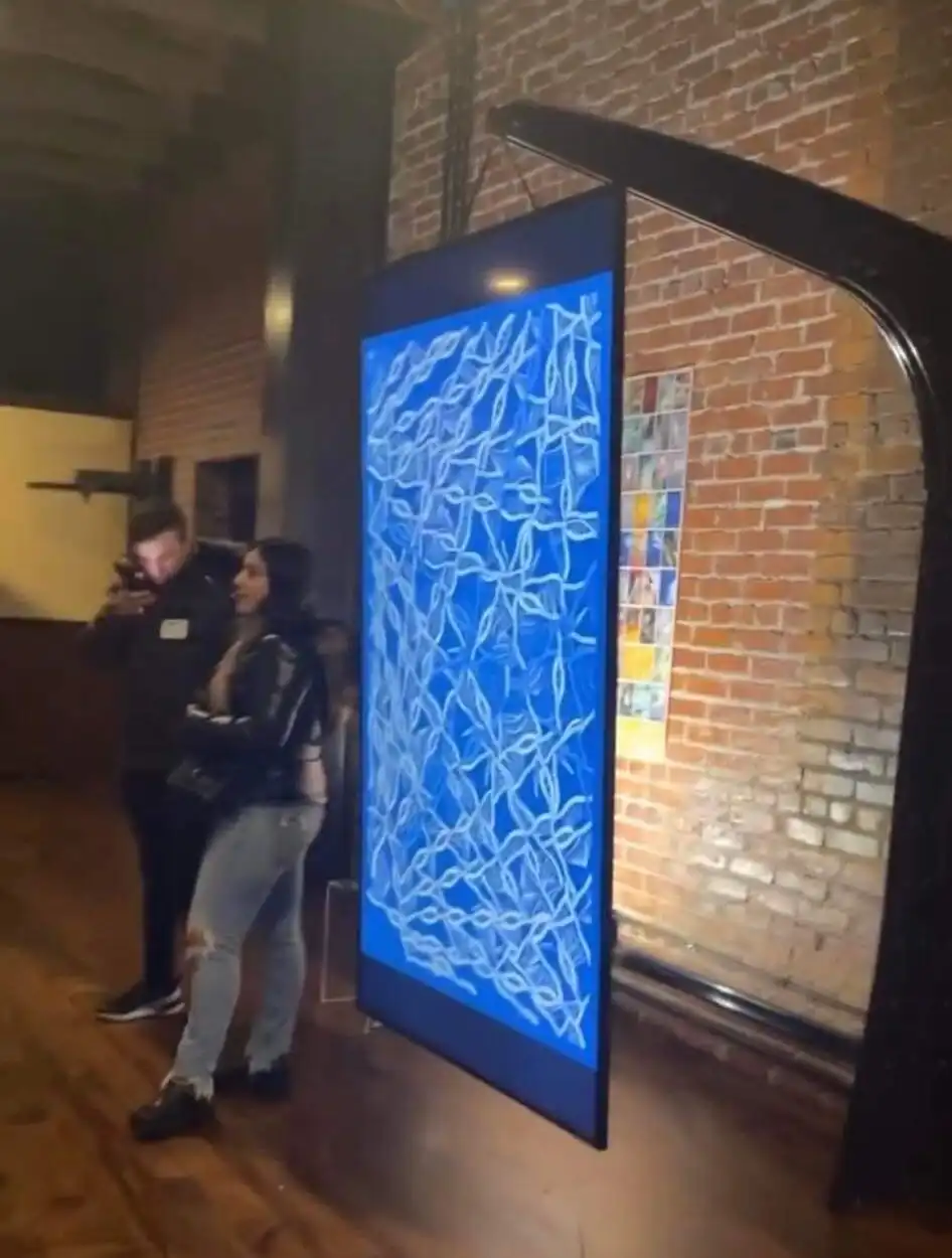 Visitors beside a hanging INTRICADA screen in a brick-walled gallery, Bright Moments Los Angeles.