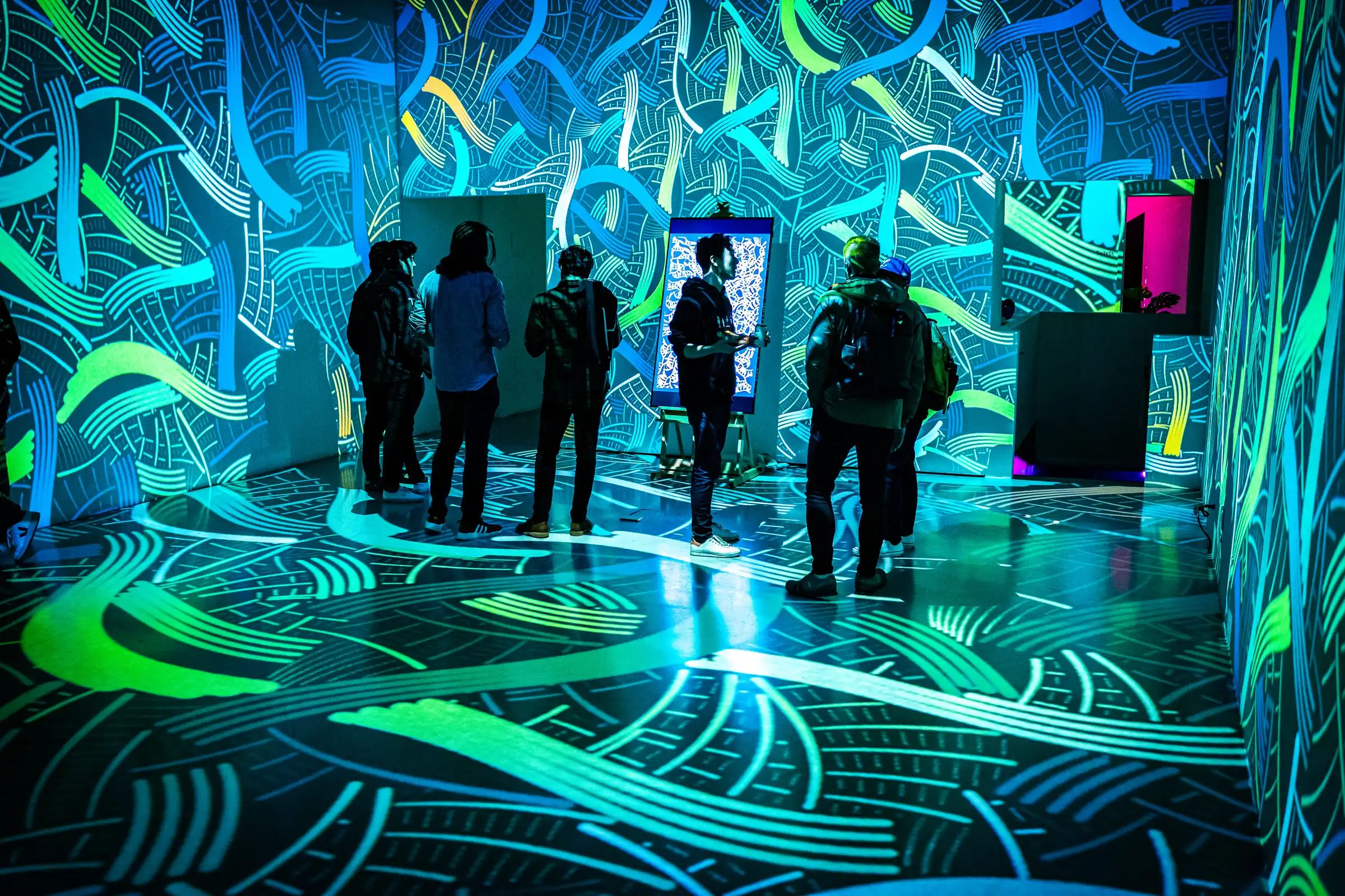 Visitors in a room covered in teal and green projected patterns, Lume Studios, New York.