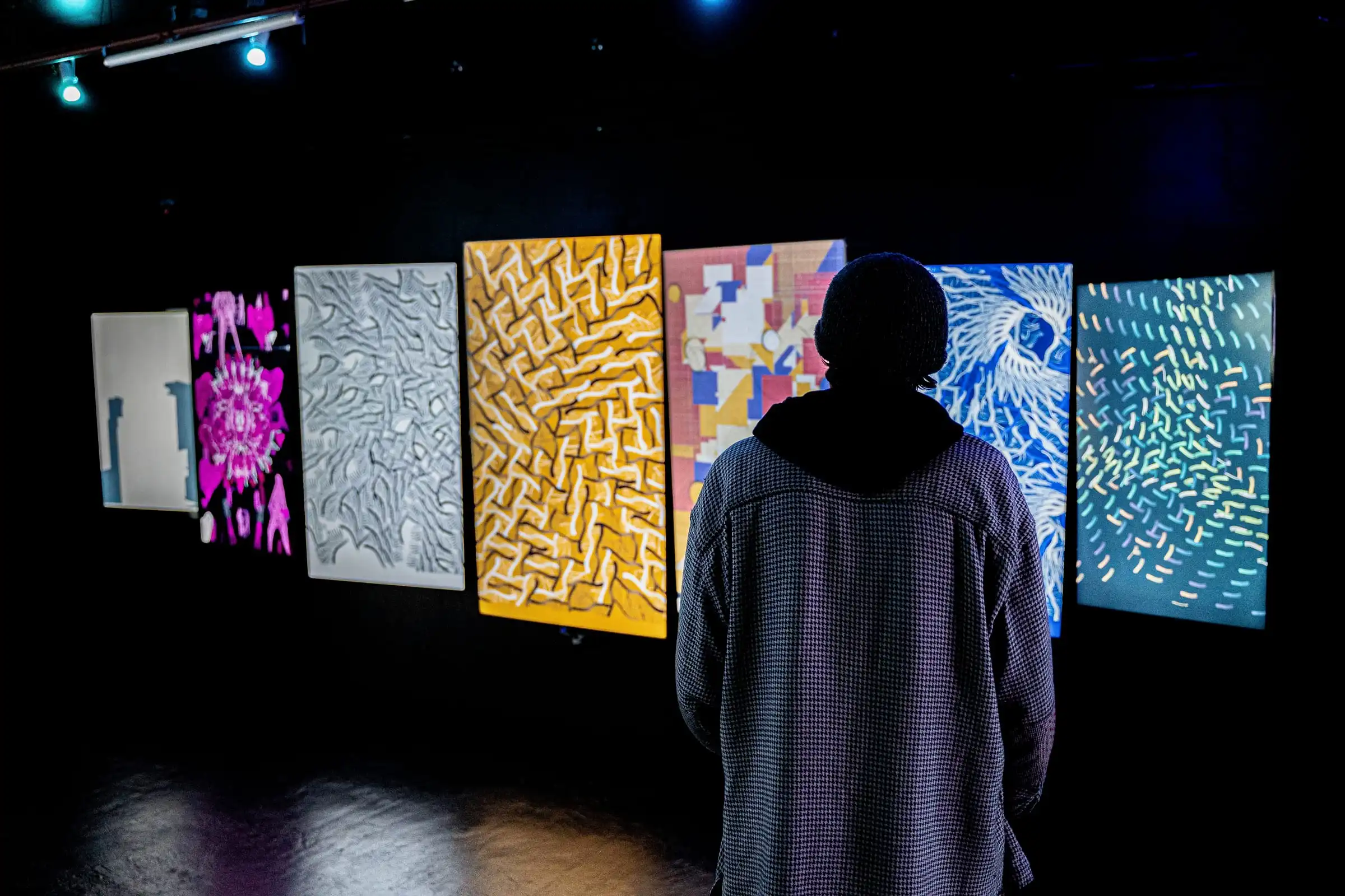 A visitor in front of a wall of screens with works by Camille Roux and other Bright Moments artists, Lume Studios, New York.