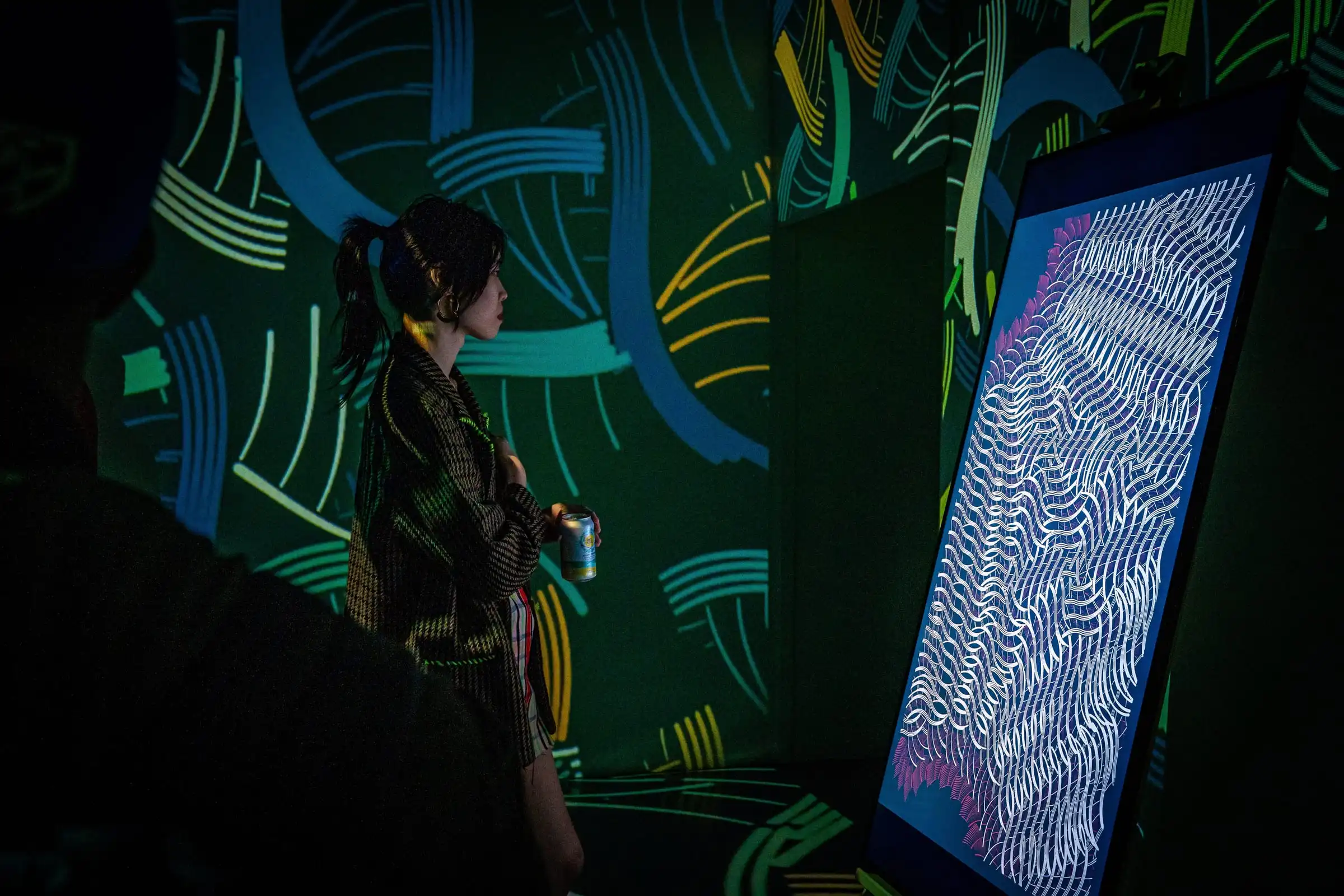 A visitor beside an INTRICADA screen, green projections behind, Lume Studios, New York.