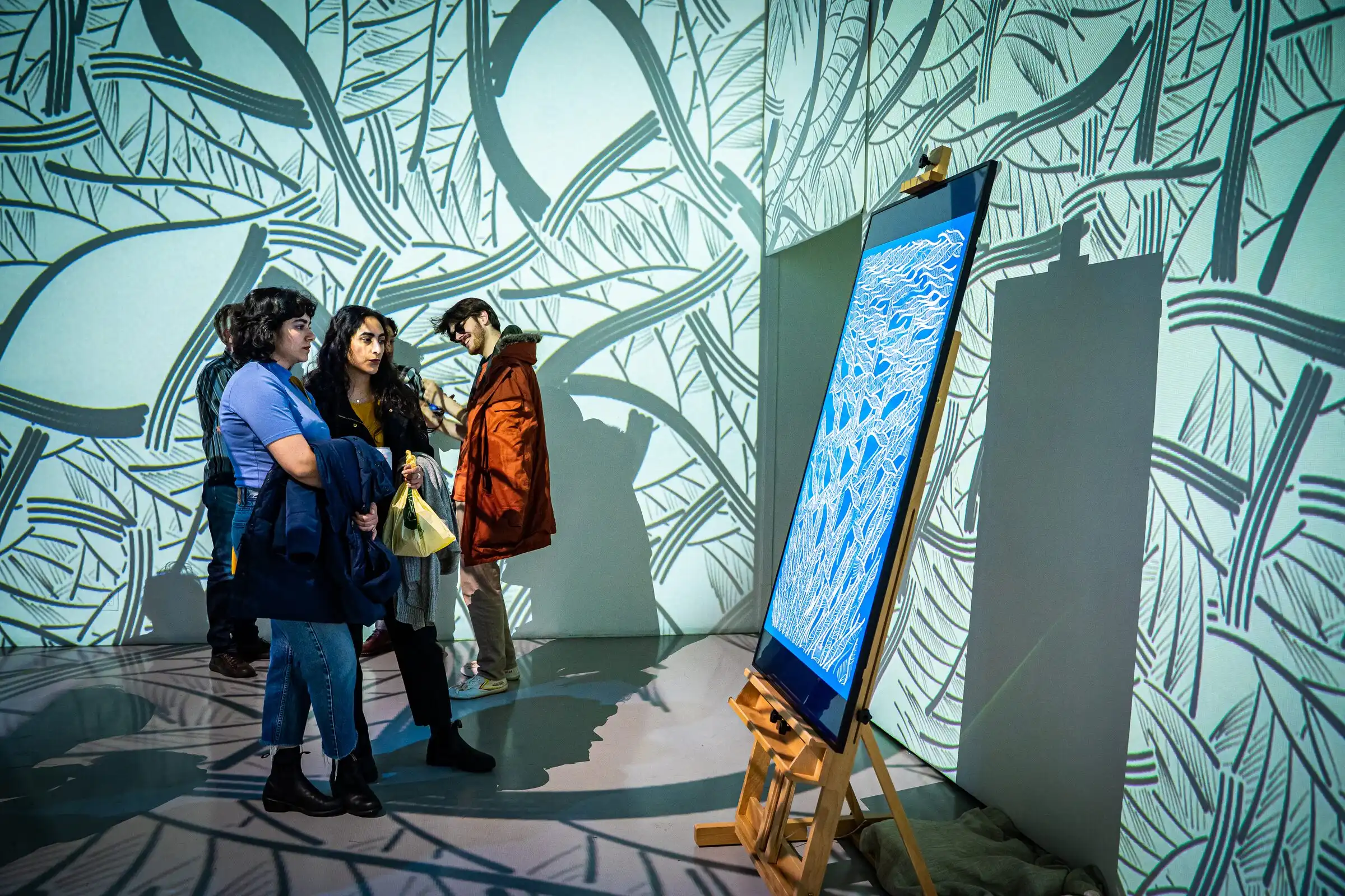 Visitors beside an INTRICADA screen on an easel in a projection-covered room, Lume Studios, New York.
